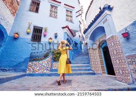 Colorful traveling by Morocco. Young woman in yellow dress walking in  medina of  blue city Chefchaouen. Royalty-Free Stock Photo #2159764503