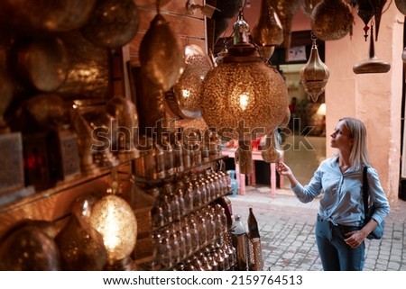 Travel and shopping. Young traveling woman with choose presents in copper souvenir handicraft shop in Morocco. Royalty-Free Stock Photo #2159764513