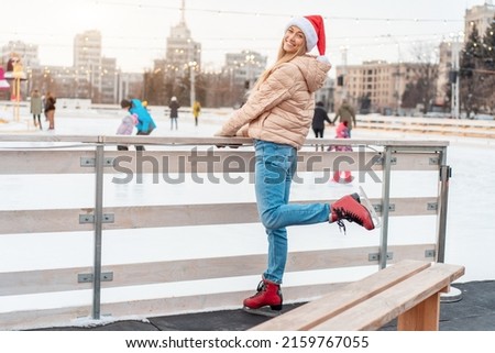 Beautiful lovely middle-aged girl blonde hair warm winter jackets knitted glove stands ice rink background Town Square. Christmas mood lifestyle Happy holiday woman walk snowy day Winter leisure