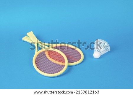 Two yellow badminton rackets and a shuttlecock on a blue background. Minimal sports concept.