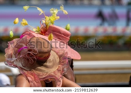 A couple of attendees at a horse race, wearing fancy hats. Royalty-Free Stock Photo #2159812639