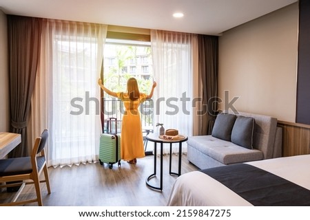 Young woman traveler opening the curtains and looking at the view from the window of a hotel room while on summer vacation, Travel lifestyle concept Royalty-Free Stock Photo #2159847275