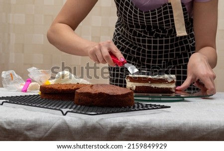 Woman's hand with kitchen spatula smoothes the cream on the second biscuit. Selective focus. Picture for articles about food, confectioners.