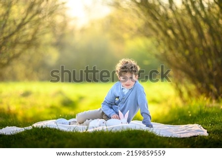 A handsome boy with blond hair is walking in the park on the meadow. Cute children and games in the park. The boy lie on the grass and play with the rabbits.