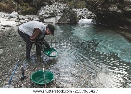 Outdoor adventures on river. Gold panning, search for gold. Man is looking for gold with a gold pan in a mountain creek Royalty-Free Stock Photo #2159865429