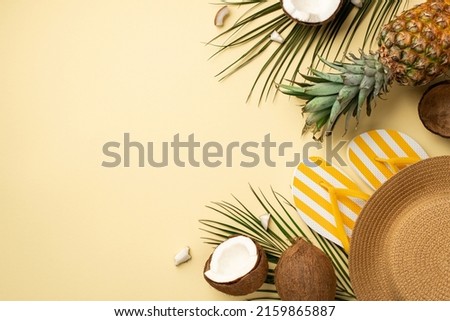 Summer weekend concept. Top view photo of yellow striped slippers sunhat tropical fruits coconuts pineapple and palm leaves on isolated beige background with copyspace
