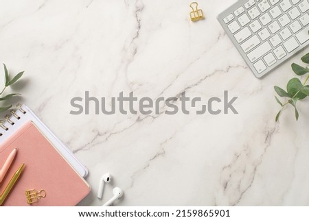 Business concept. Top view photo of workstation keyboard pink organizers wireless earbuds pens gold binder clips and eucalyptus branches on white marble background with blank space