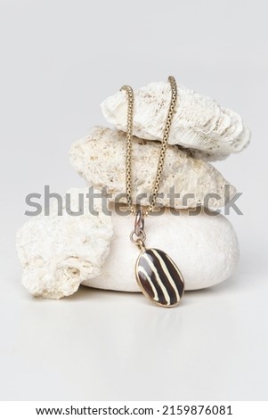Jewelry fashion photography. Gold necklace with pendant displayed on decorative stones, studio product shot.