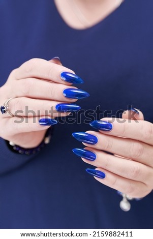 Woman's beautiful hand with long nails and bright blue manicure with bottles of nail polish