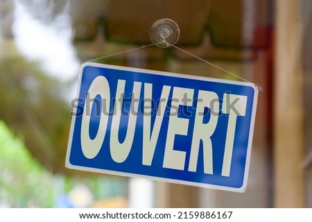 Close-up on a blue sign in the window of a shop displaying the message in French - Ouvert - meaning in English - Open -.