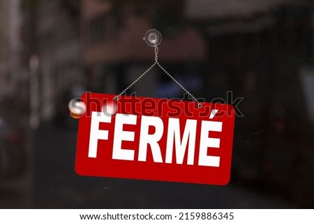 Close-up on a red sign in the window of a shop displaying the message in French - Fermé - meaning in English - Closed -.