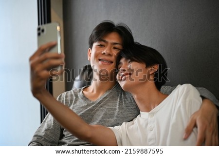 Asian teen gay couple taking a selfie together in living room, partner hand is around his lover, showing some LGBT affection. LGBT concept