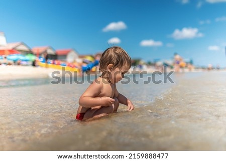 Little funny funny kid, collects shells and pebbles in the calm blue sea on a sandy bottom under the hot summer sun on a bright vacation