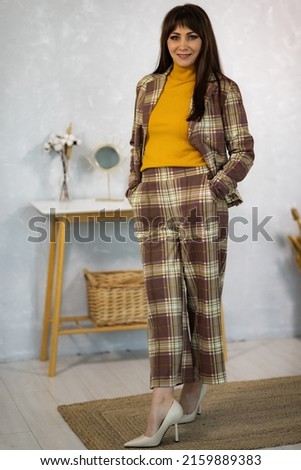 Model in a pantsuit and golf and a notebook in her hands against a gray wall in the studio