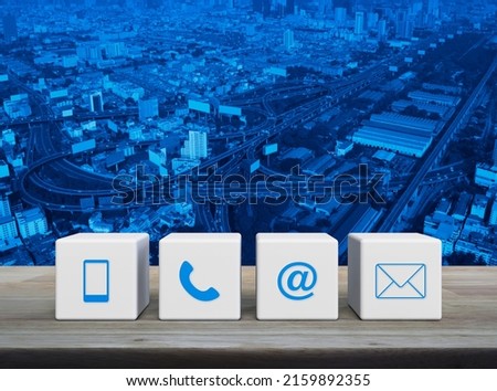 Mobile phone, telephone, email address and mail icon on white block cubes on wooden table over modern city tower, street, expressway and skyscraper, Business customer service and support online