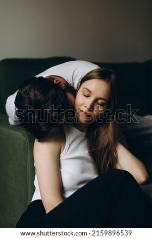a dark-haired young man tenderly kisses the neck of a blonde-haired young woman indoors. young loving couple. beautiful woman closed her eyes from enjoying the kiss