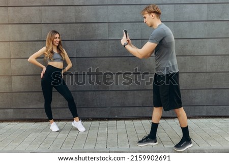 Picture of a sporty handsome man taking pictures of his girlfriend outdoors on the wall. Sport