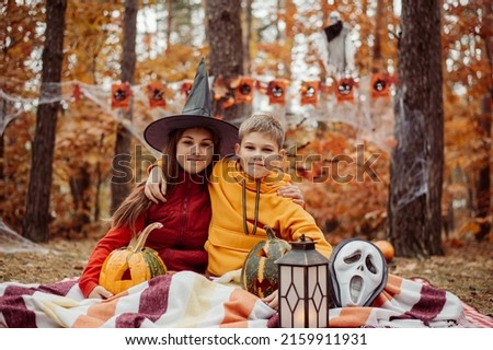 Little boy and girl on picnic pad in forest, halloween decorations around. Celebrating Halloween