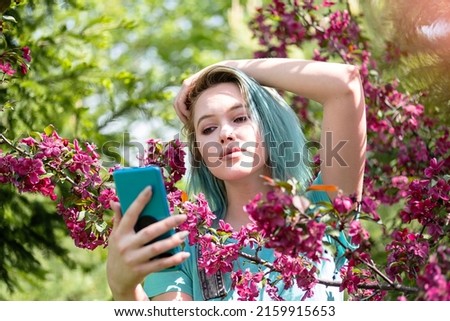 Blue haired woman taken selfie against spring blossom tree.