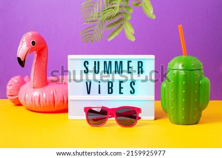 Inflatable flamingo for drink, pink sunglasses, cactus mug and lightbox with quote Summer Vibes on bright background. Retro vibe or 80s, nostalgic style, retro aesthetic still life. Summer vacation vi