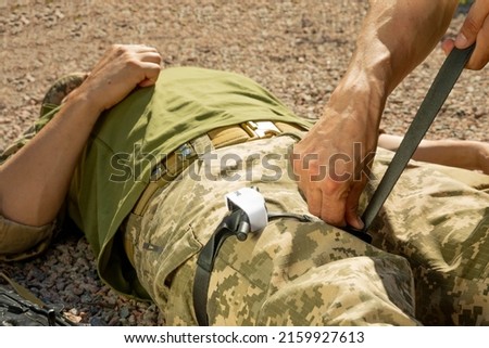 Army medics practice applying a tourniquet to the leg of a wounded soldier. Combat tactical equipment. Combat use Turnstile. The concept of military medicine. Royalty-Free Stock Photo #2159927613