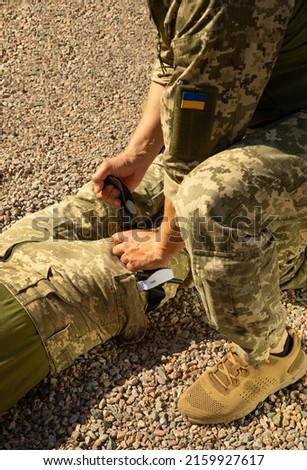 Army medics practice applying a tourniquet to the leg of a wounded soldier. Combat tactical equipment. Combat use Turnstile. The concept of military medicine. Royalty-Free Stock Photo #2159927617