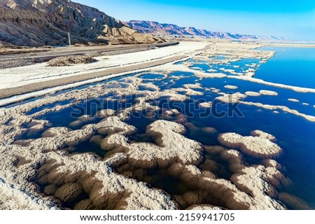 The blue water is surrounded by pink mountains. The picturesque Dead Sea is covered with patterns of salt. The picture was taken by a drone from a aerial view. Israel. Winter sunny day. 