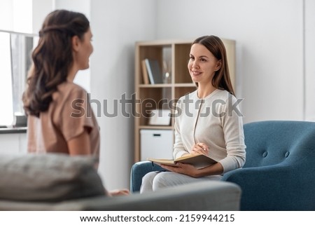 psychology, mental health and people concept - smiling psychologist with notebook and woman patient at psychotherapy session Royalty-Free Stock Photo #2159944215