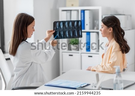 medicine, healthcare and people concept - female doctor or vertebrologist showing x-ray image of spine to woman patient at hospital Royalty-Free Stock Photo #2159944235