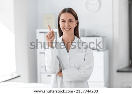 medicine, healthcare and profession concept - smiling female doctor pointing finger up at hospital Royalty-Free Stock Photo #2159944283