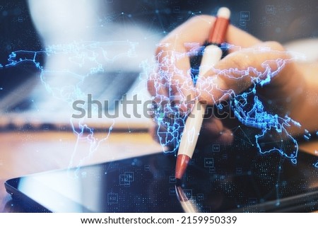 Close up of hands using digital tablet with pen and laptop with glowing blue map hologram and digital data concept on blurry office desktop background. Info, news and planet concept. Double exposure
