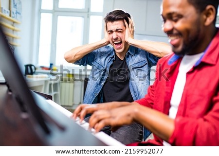 upset caucasian handsome musician man discontent singing, and teaching to play on piano of african american man