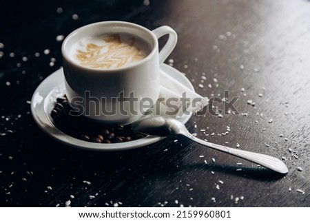 White cup of hot tasty coffee stands on table with coffee beans