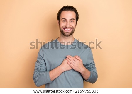 Photo of young cheerful man arms on chest pray hope appreciate thankful isolated over beige color background