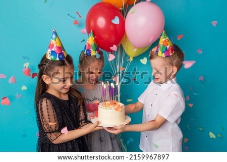 Two little girls and boy blowing candles on cake, happy birthday party.