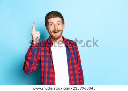 Ideas. Emotional young red-headed man in white t-shirt and plaid shirt posing isolated on blue background. Concept of art, fashion, emotions, aspiration. Copy space for ad