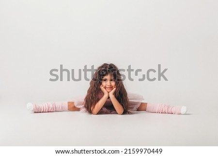 Little swarthy ballerina dancer in a pink tutu academy student posing on white background 