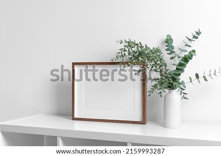 Wooden frame mockup in white room interior with fresh eucalyptus plant in vase, copy space for artwork, print or photo presentation