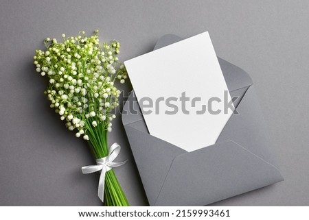 Invitation or greeting card mockup with envelope and lily of the valley flowers, flat lay with copy space