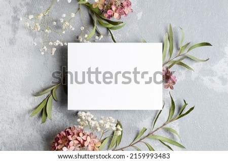 Wedding invitation or greeting card mockup with eucalyptus, gypsophila and hydrangea decorations. Card mockup with copy space on grey.