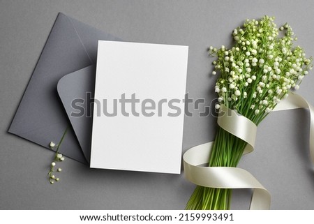 Invitation or greeting card mockup with envelope and lily of the valley flowers on grey background, blank card with copy space