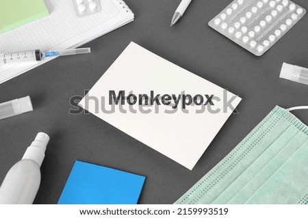 The word Monkeypox on Gray modern doctor desk table background. Mask, notepad, syringe, sanitizer and supplies. Monkeypox spreading. Medicine and healthcare, medical education. Top view.