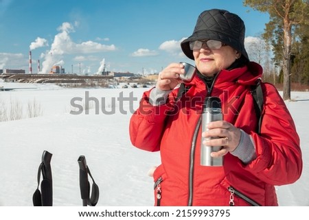 Elderly woman drinks coffee in winter nature.