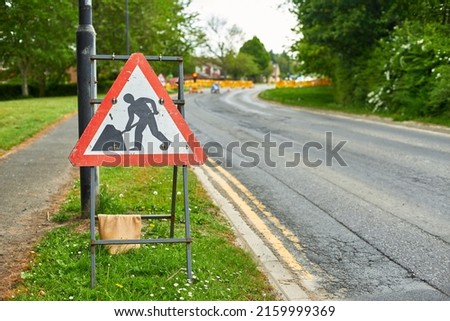 A roadwork sign against the backdrop of a broken road. Repair work of the road is underway. Repair of the street marked with a red sign.