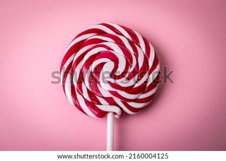 Red and white lollipop on a pink background.