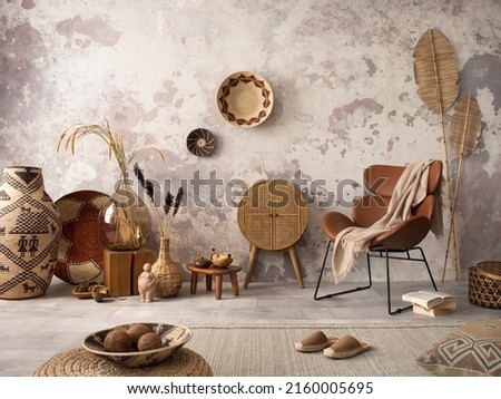 The stylish ethnic composition at living room interior with design brown armchair, colorful baskets, rattan sideboard and elegant personal accessories. Grey concrete wall. Cozy apartment. Home decor.  Royalty-Free Stock Photo #2160005695