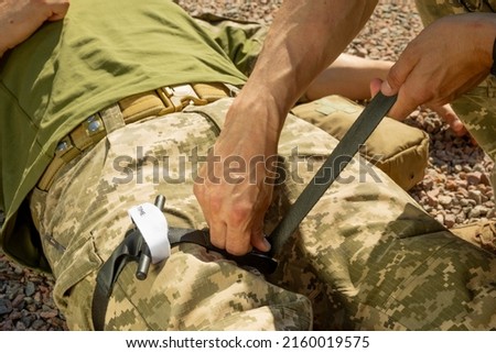 Army medics practice applying a tourniquet to the leg of a wounded soldier. Combat tactical equipment. Combat use Turnstile. The concept of military medicine. Royalty-Free Stock Photo #2160019575