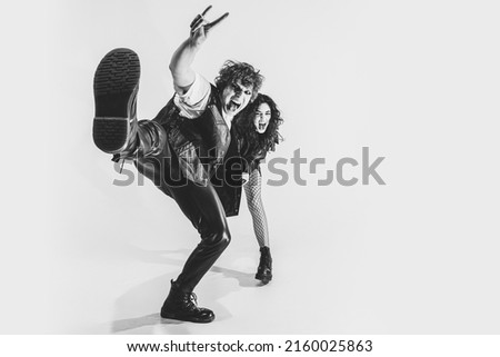 Wide angle view. Monochrome portrait of crazy musicians, young boy and girl wearing black leather outfits moving on white studio background. Concept of style, art, fashion and youth, ad Royalty-Free Stock Photo #2160025863
