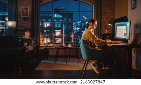 Young Couple Spending Time at Home, Working on Computers from Their Stylish Loft Apartment in the Evening. Female Resting on the Sofa and Browsing Social Media on Laptop. Man Designing UX Interface. Royalty-Free Stock Photo #2160027847