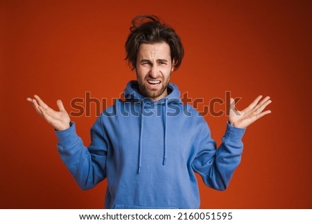 Young disheveled man grimacing and gesturing at camera isolated over red background Royalty-Free Stock Photo #2160051595